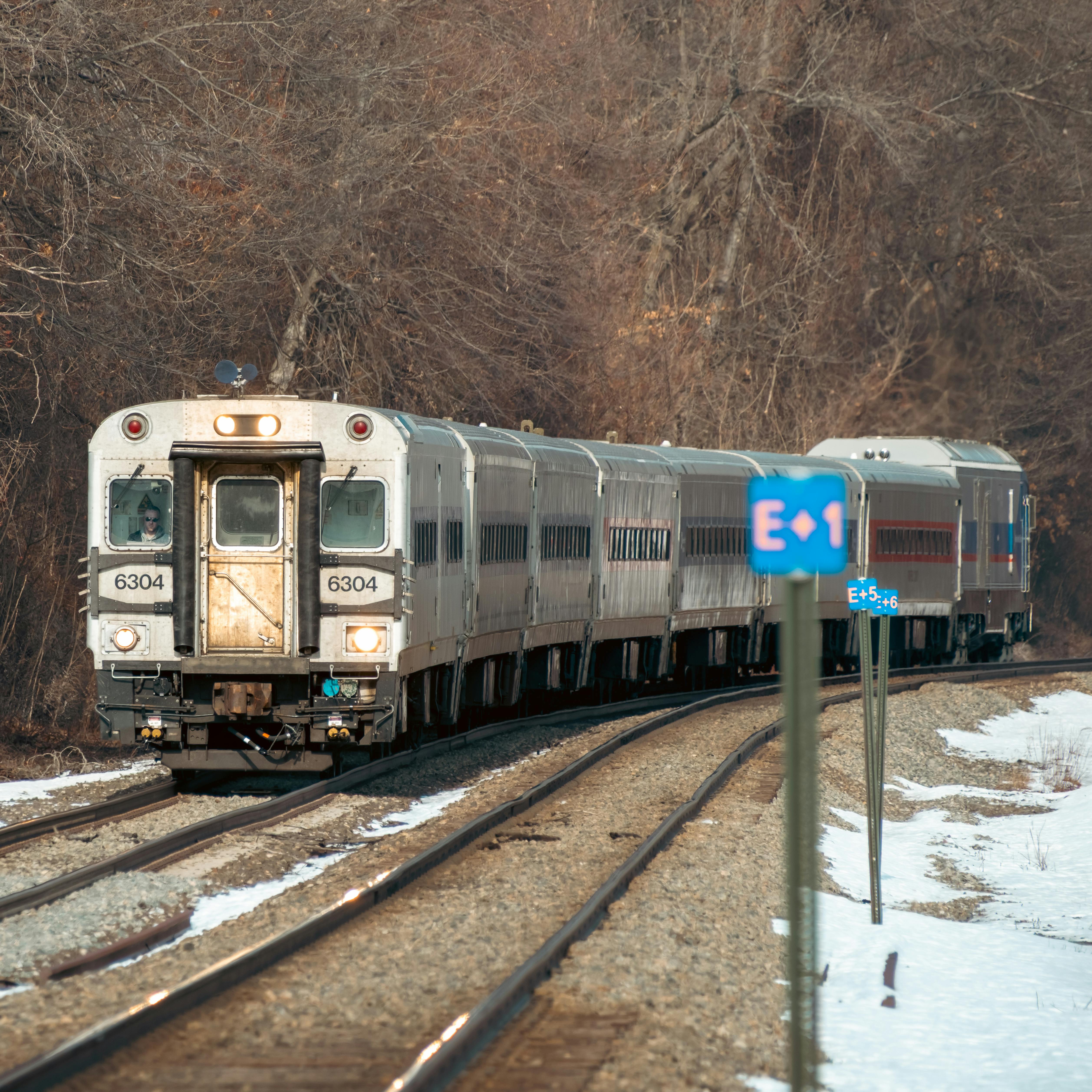 бесплатная Пригородный поезд, движущийся по заснеженному зимнему пейзажу, демонстрирующий стальные рельсы и изогнутые пути. Стоковое фото