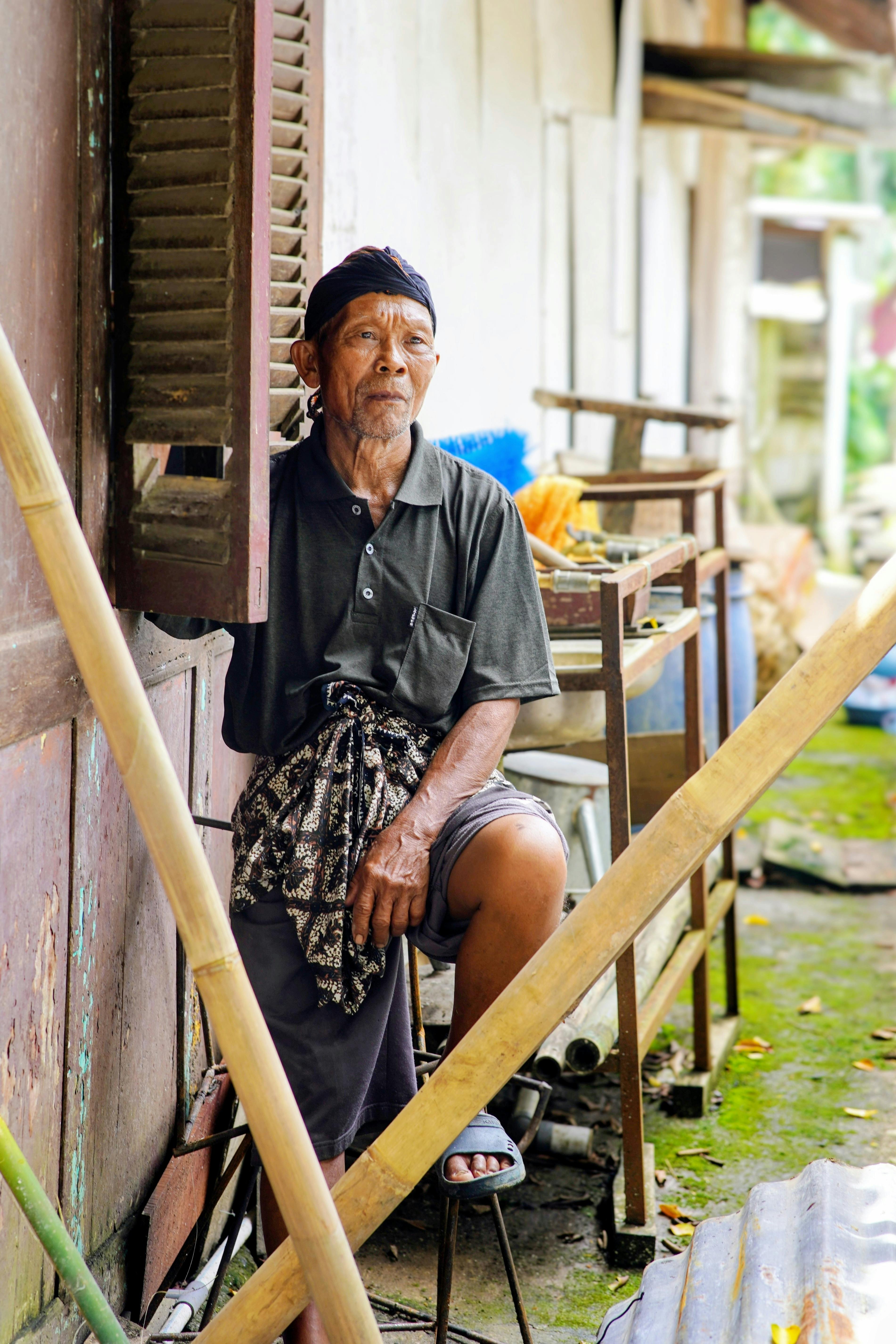 бесплатная Пожилой мужчина в традиционной одежде задумчиво сидит перед сельским домом. Стоковое фото