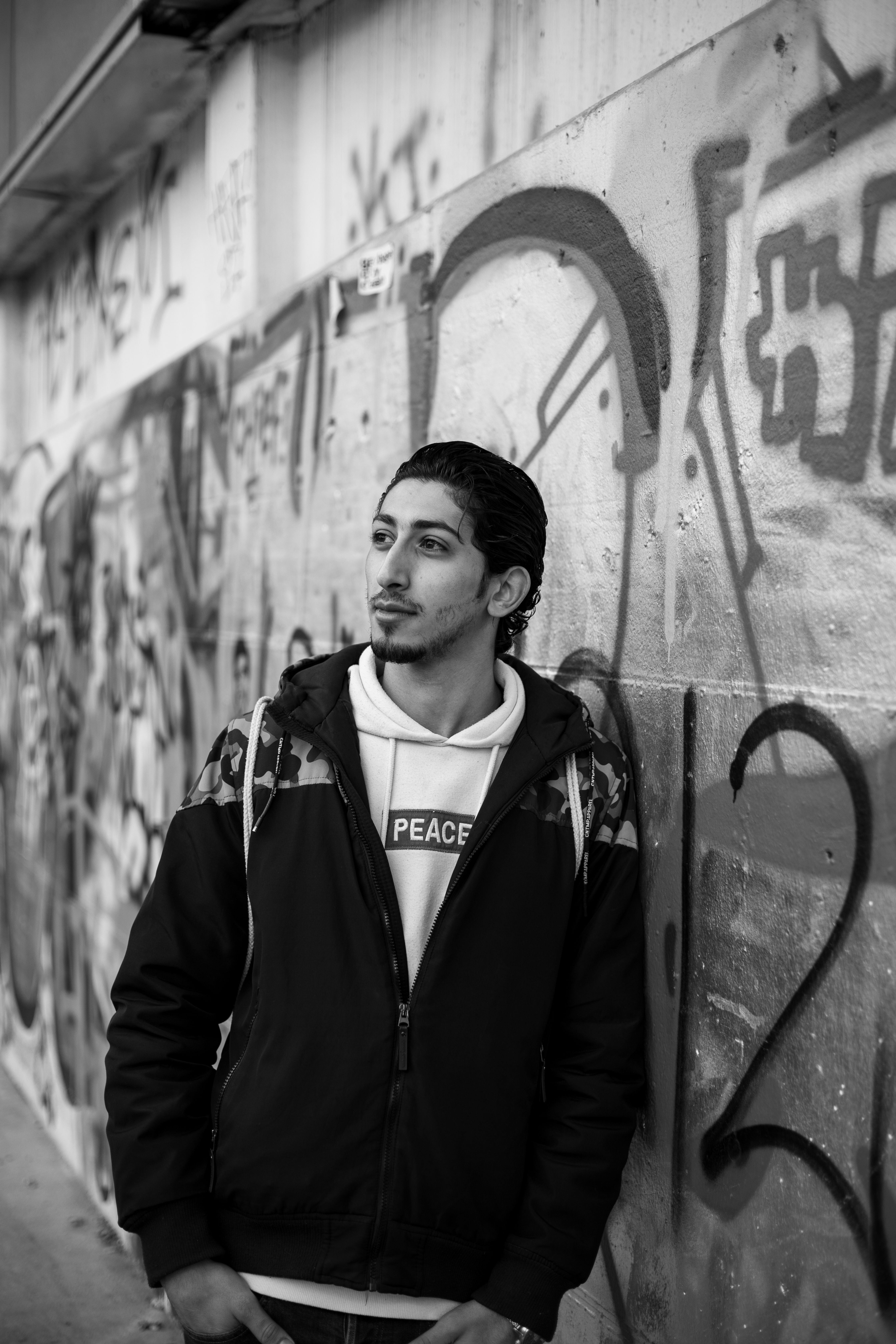 Black and white portrait of a young man posing by graffiti in Graz, Austria.