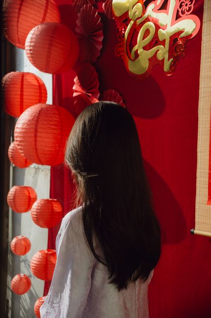 Young girl in white observing a red festive decoration for Lunar New Year.