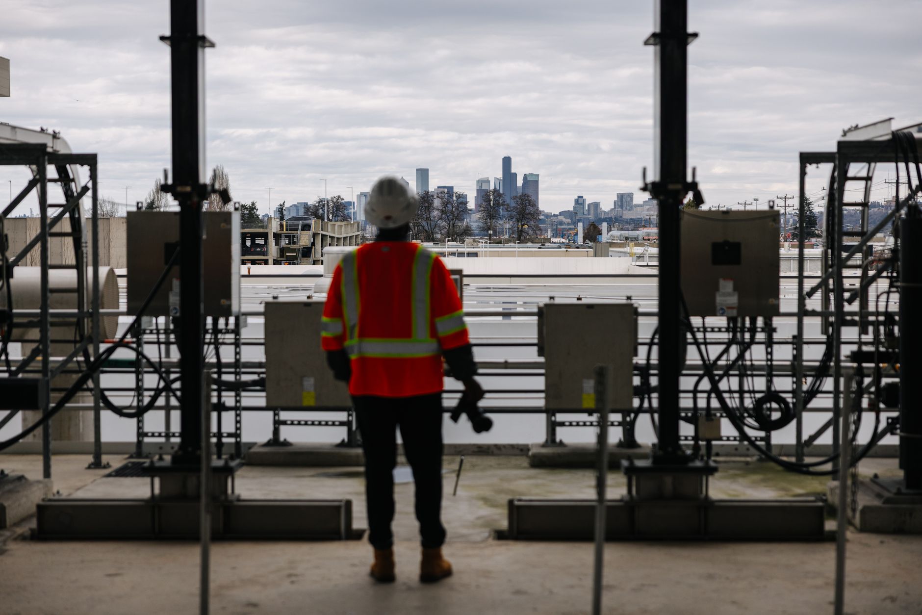 A construction worker in safety gear overlooks a modern city skyline from a high vantage point.