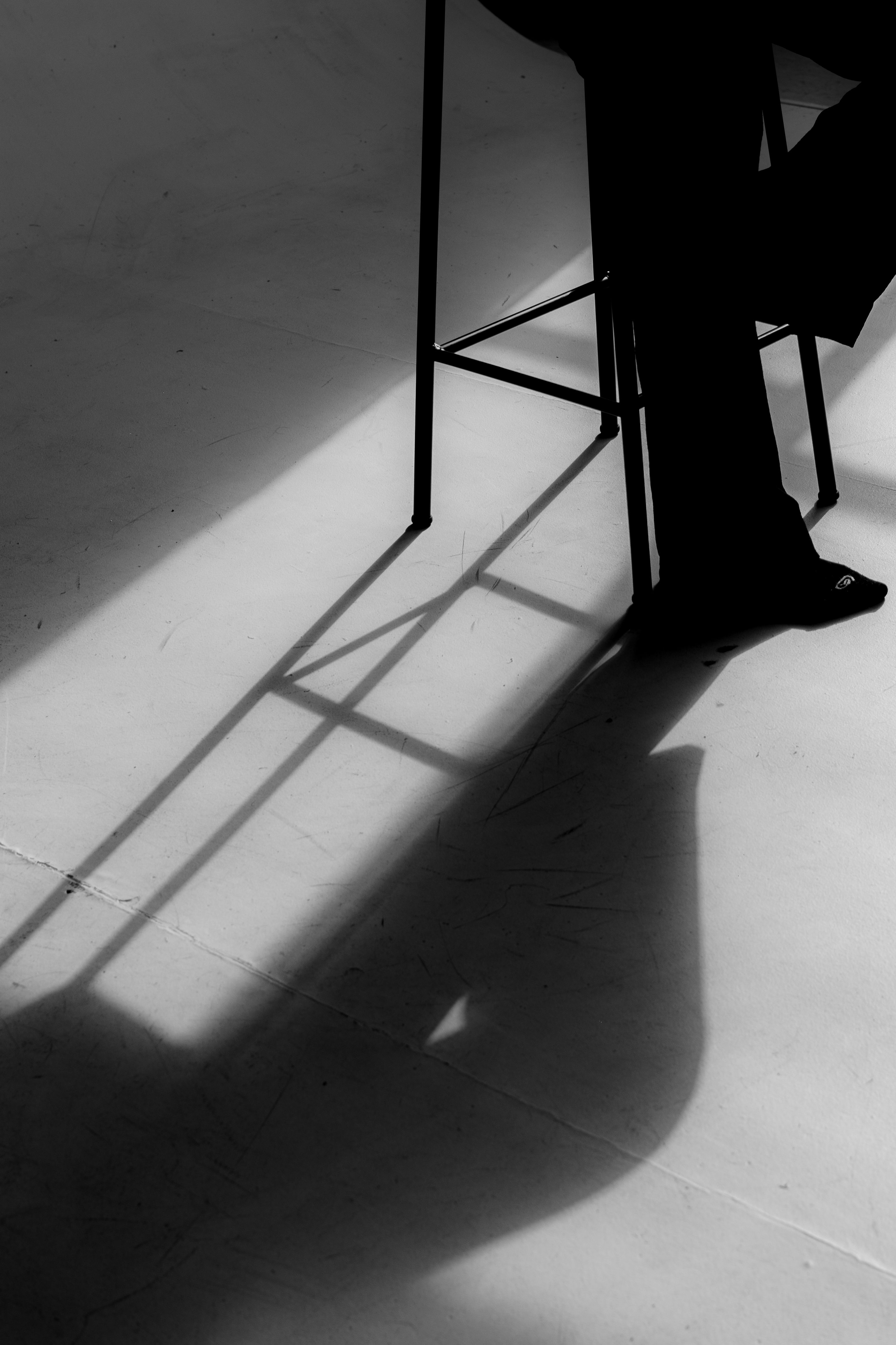 Fotomural Foto artística en blanco y negro que destaca las sombras en el suelo de una silla y una persona.