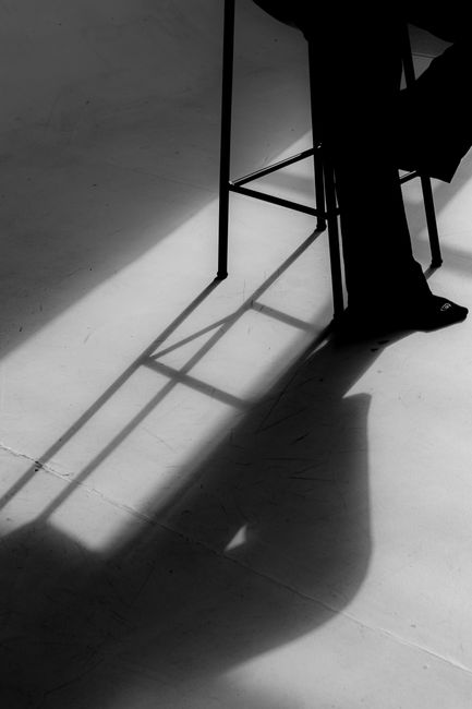 Fotomural Foto artística en blanco y negro que destaca las sombras en el suelo de una silla y una persona.