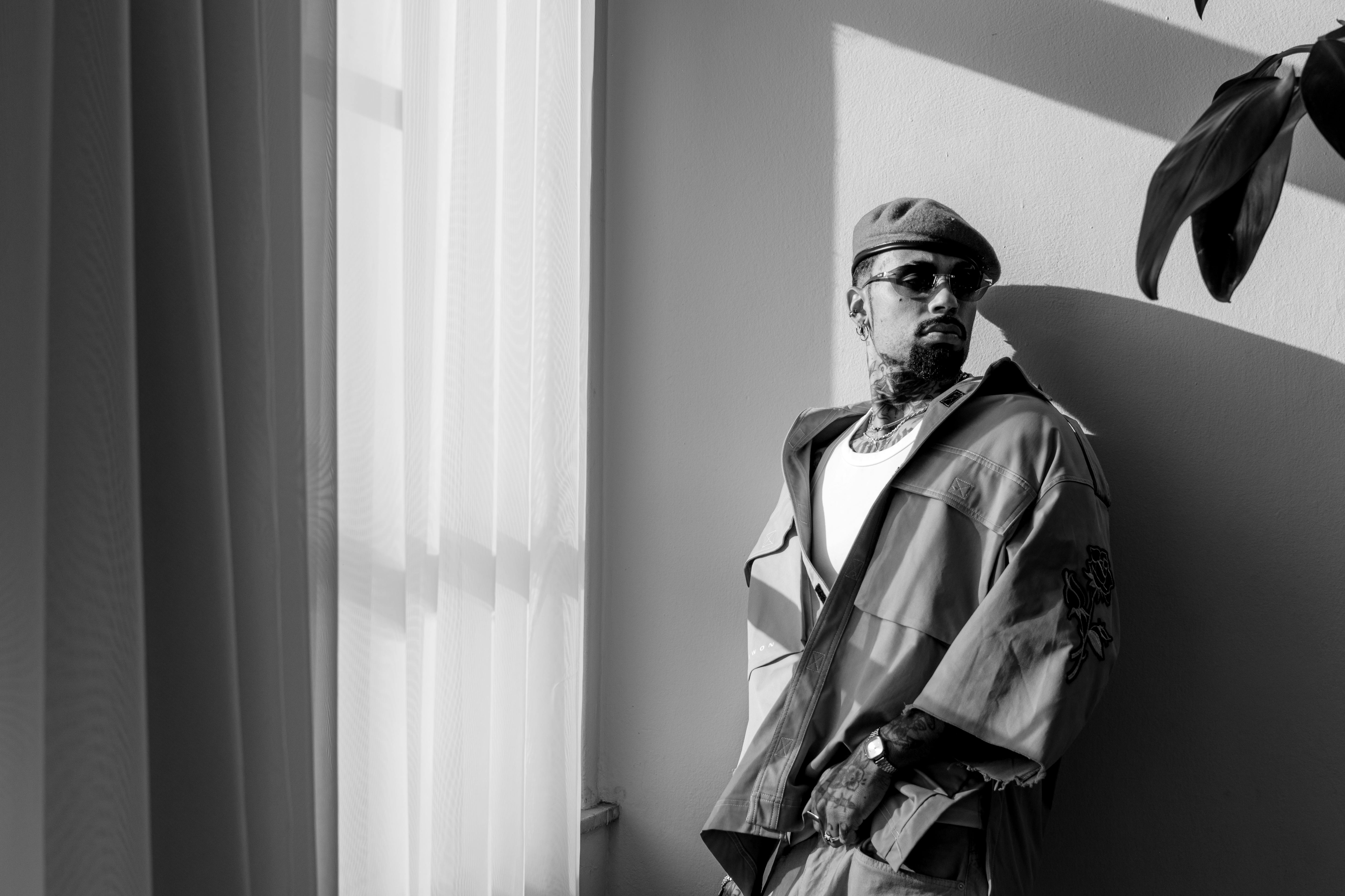 Free Black and white portrait of a stylish man leaning by a window, exuding urban fashion. Stock Photo