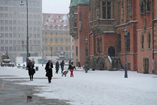 Snowy city scene with people walking near historic buildings.