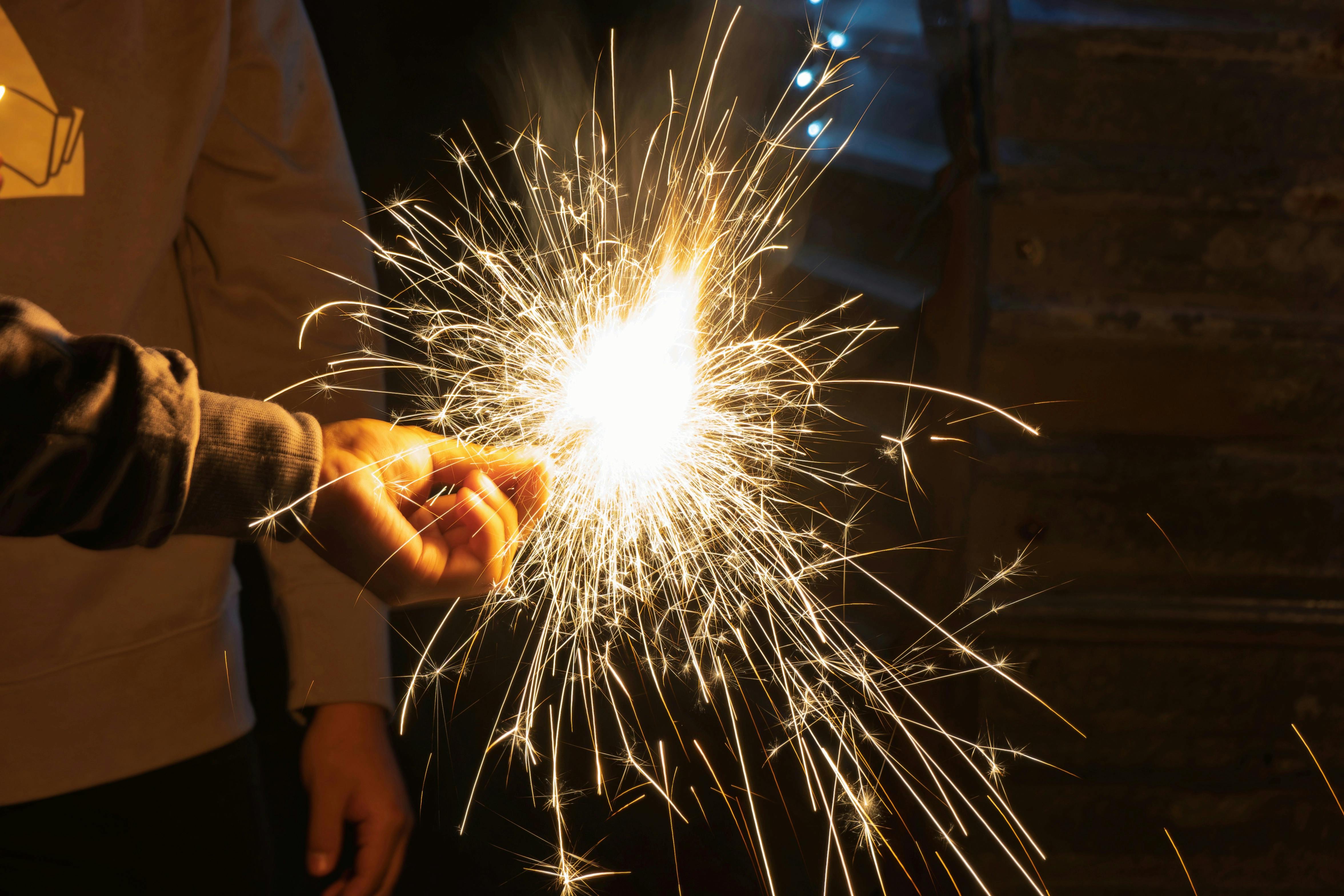 A close-up of a hand holding a bright sparkler at night, creating fireworks.