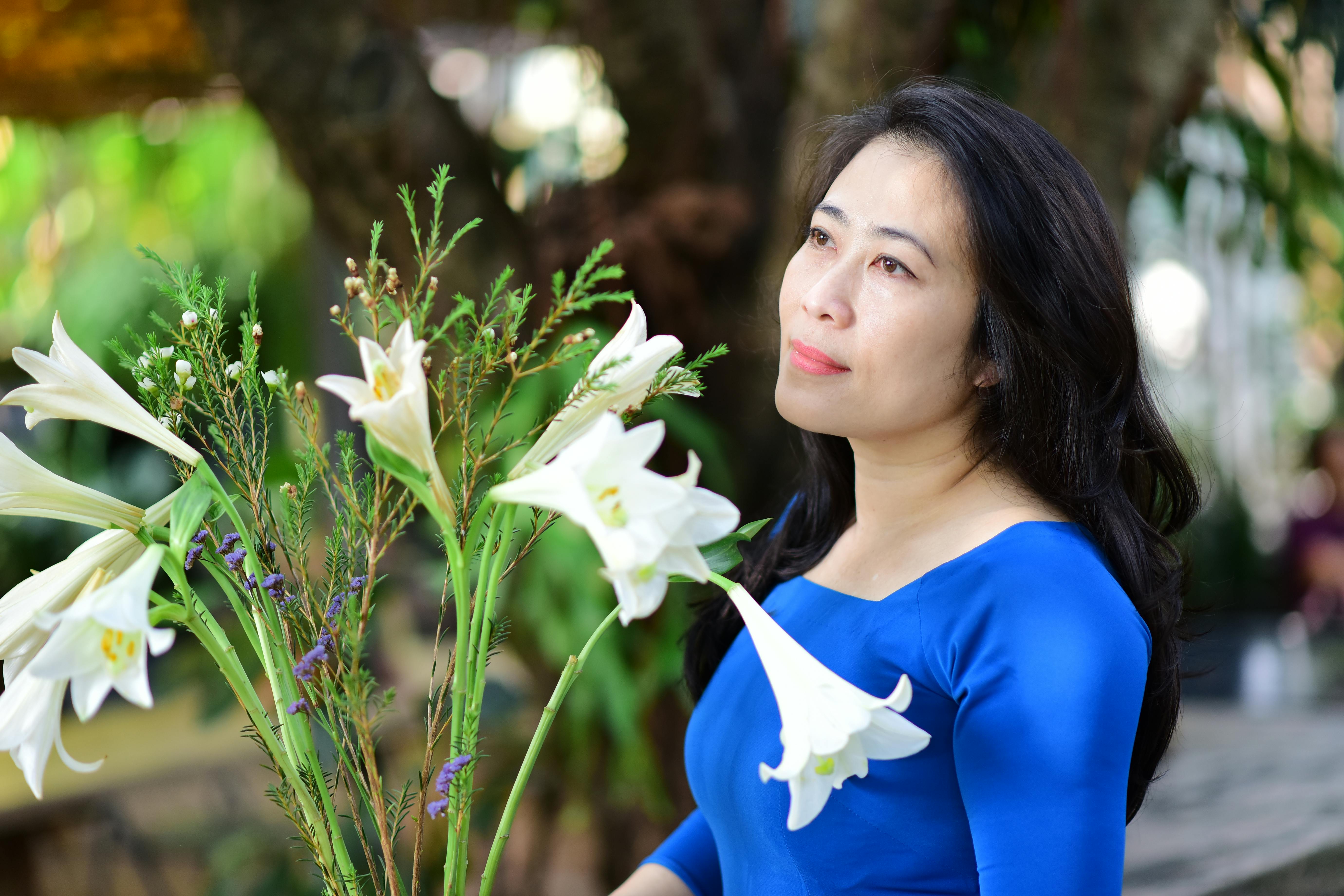 Woman in a blue dress holding a bouquet of white lilies outdoors, looking thoughtful.
