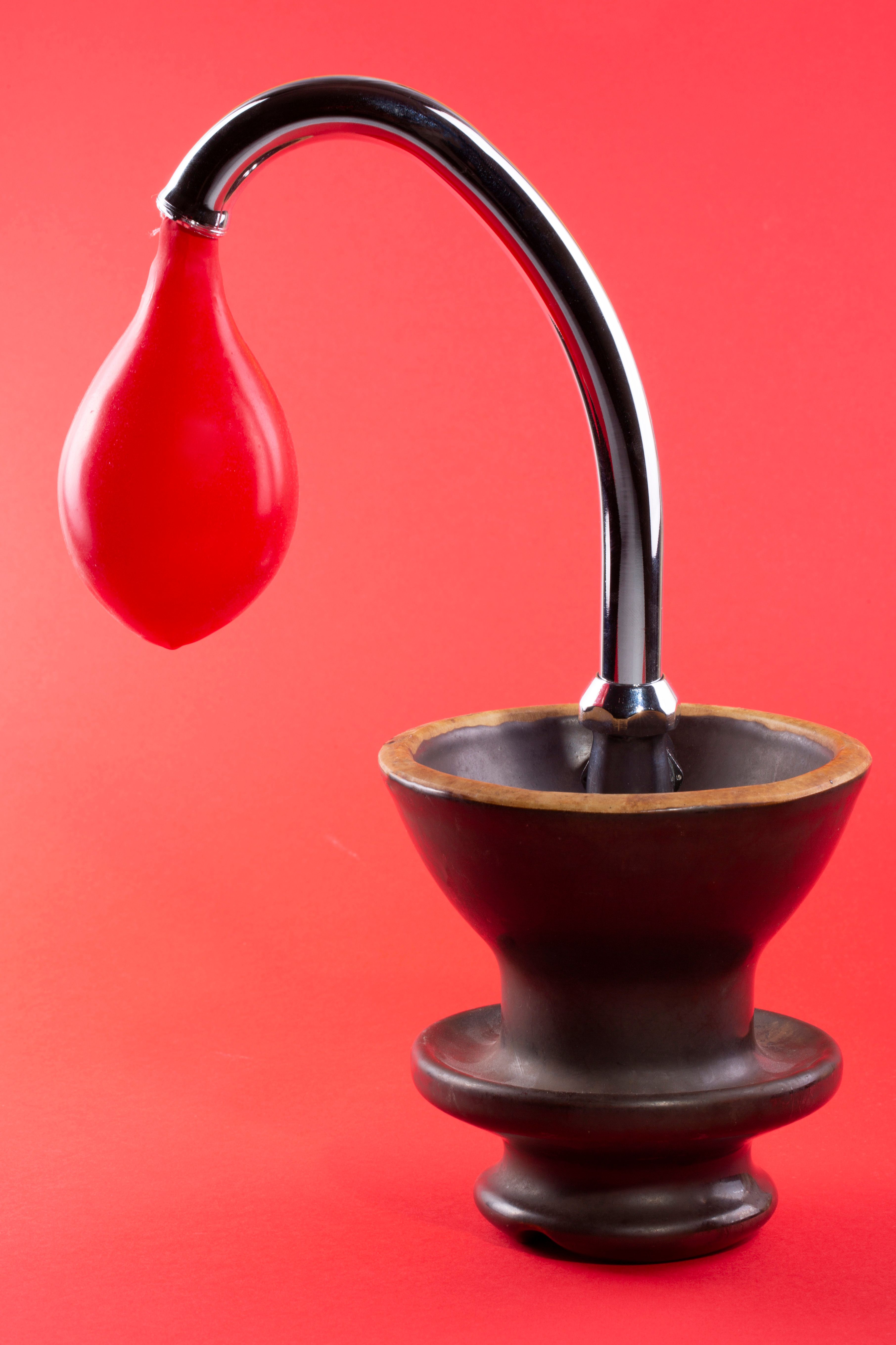 Red rubber bulb attached to a chrome pipe over a wooden base set against a red background.