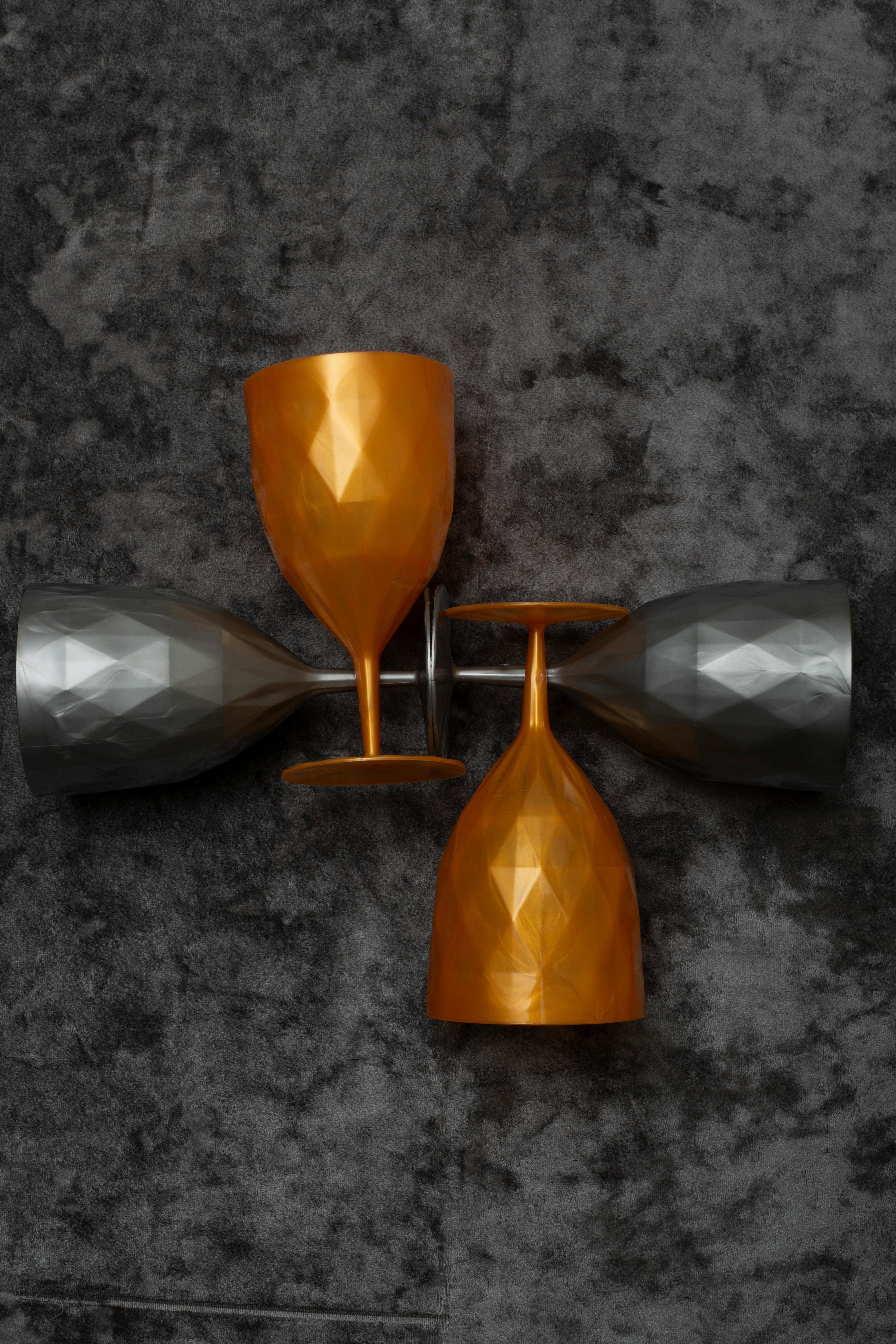 Gratis Quattro bicchieri da vino metallici con motivi geometrici su uno sfondo grigio testurizzato. Foto a disposizione