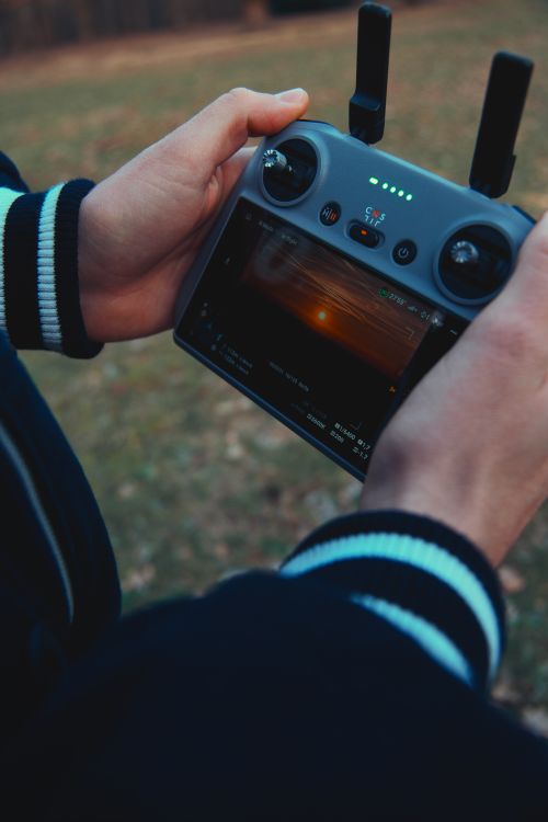 Free Close-up of hands holding a drone remote control with screen display outdoors. Stock Photo