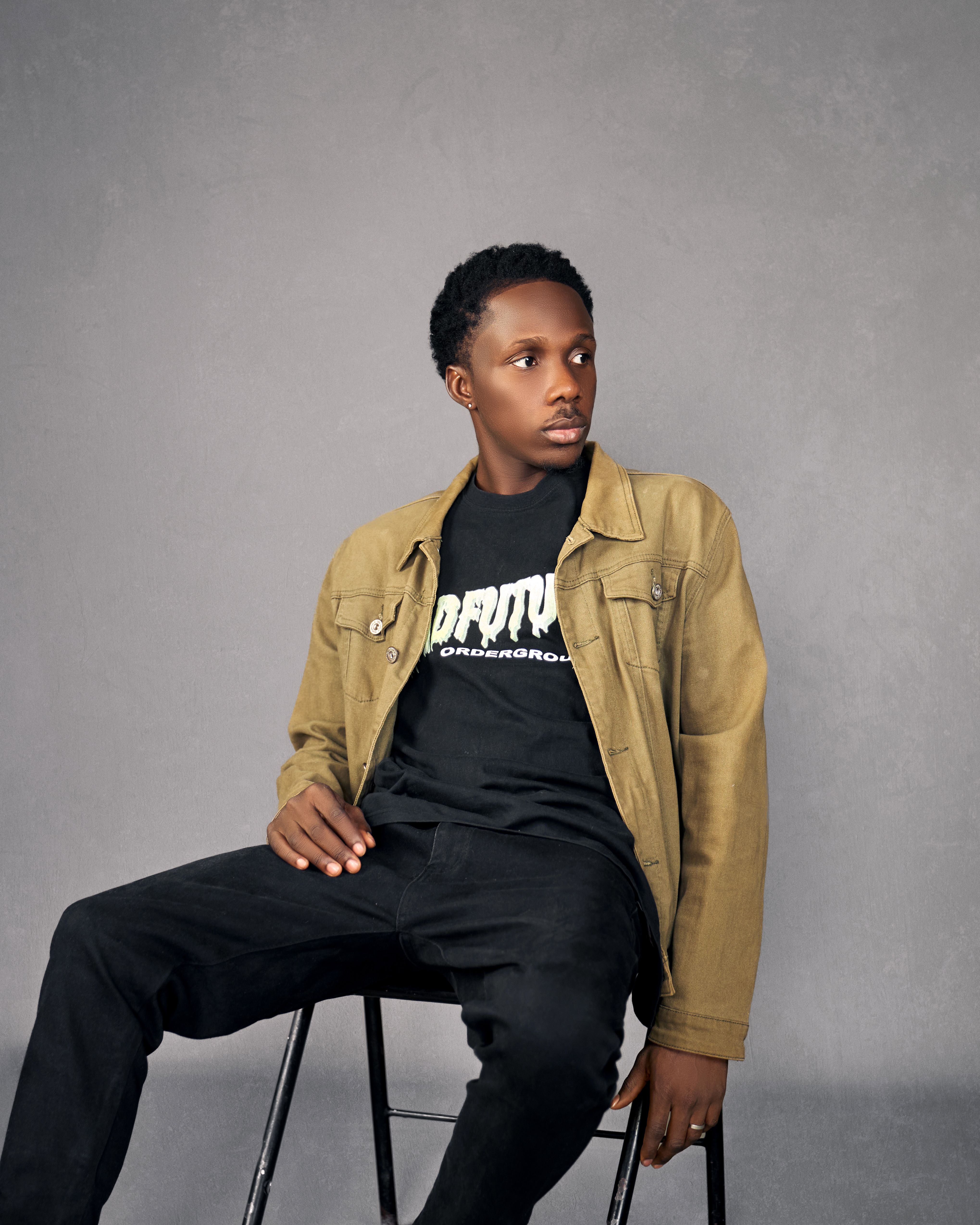 Stylish portrait of a young man sitting against a neutral background, exuding confidence.