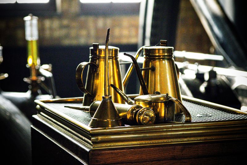 A collection of vintage metal oil cans displayed on a wooden table in an industrial setting.