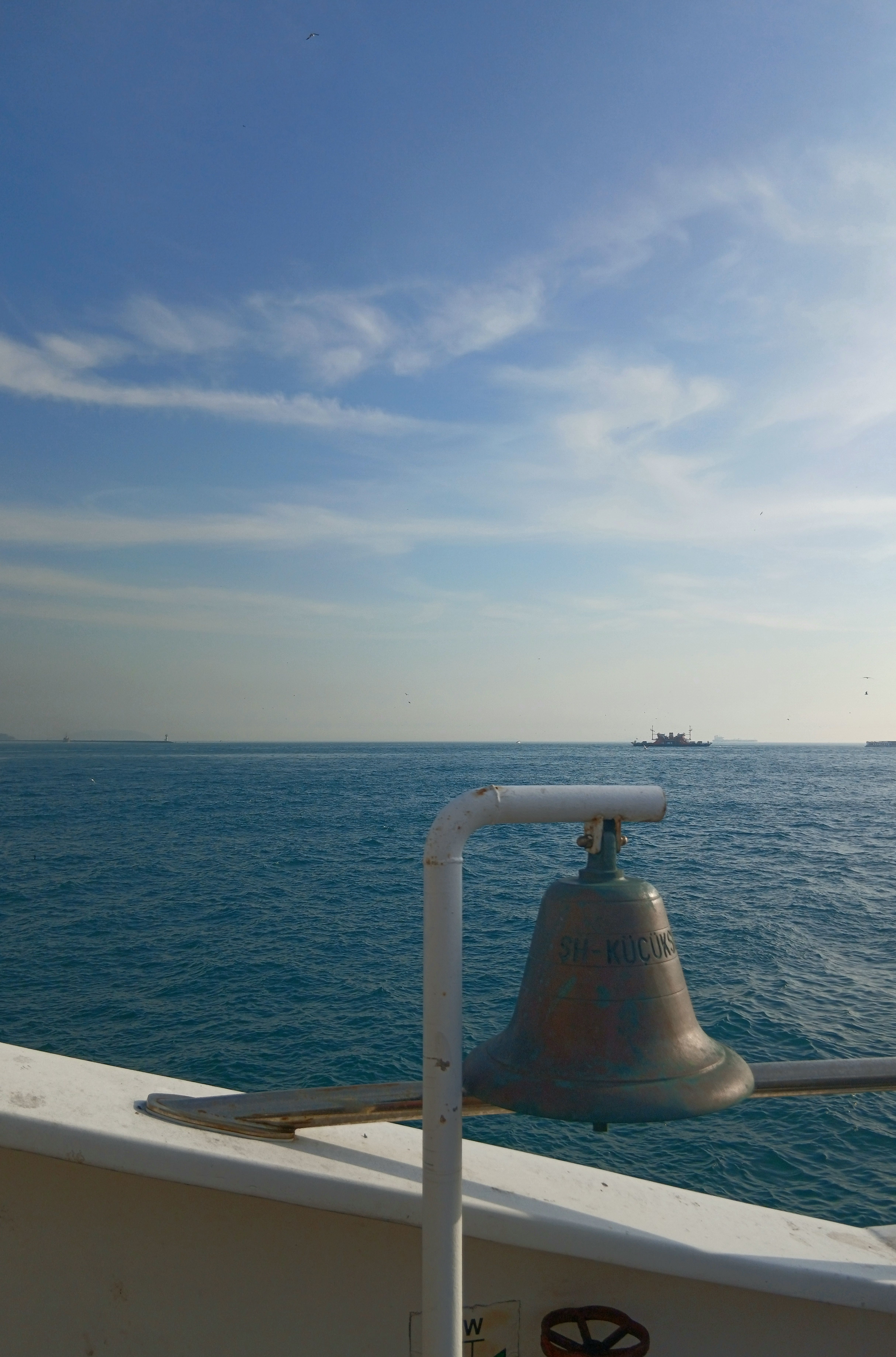 Scenic view of a ship's bell against a blue sea and sky, with distant ships on the horizon.