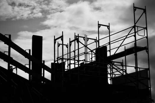 Black and white image of construction scaffolding silhouette with dramatic cloudy sky.