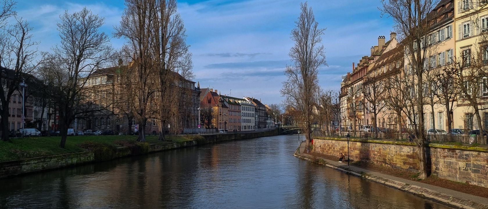 Canal de Strasbourg bordé d'immeubles anciens et d'arbres dénudés, sous un ciel clair d'hiver.
