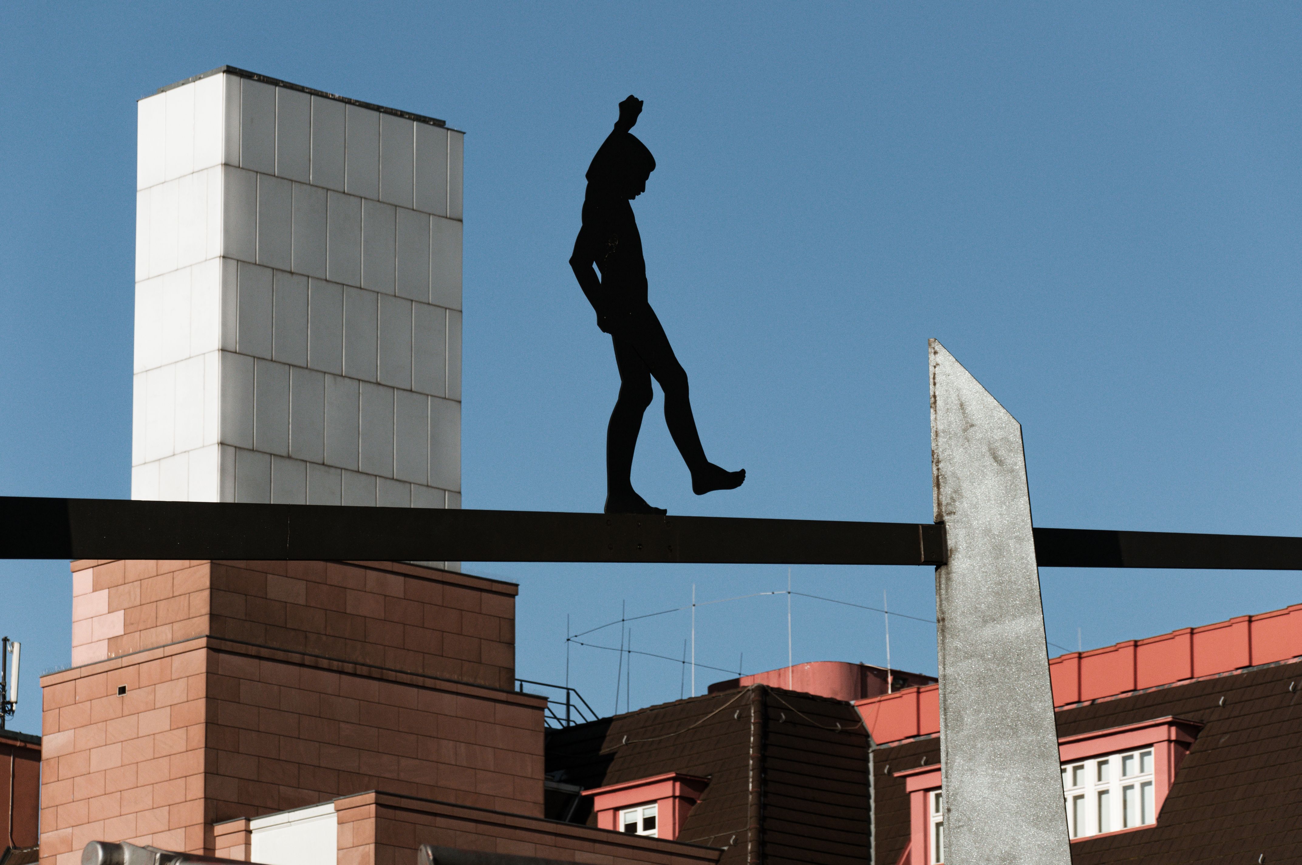 Modern sculpture silhouette set against a clear blue sky in urban architectural setting.