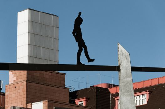 Modern sculpture silhouette set against a clear blue sky in urban architectural setting.