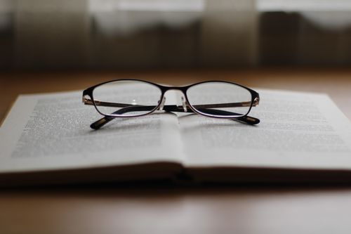 Free A pair of reading glasses resting on an open book, creating a cozy reading ambiance. Stock Photo