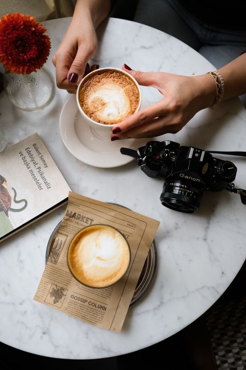 Free Overhead view of a coffee shop table with a cappuccino, latte art, vintage camera, book, and flower. Stock Photo