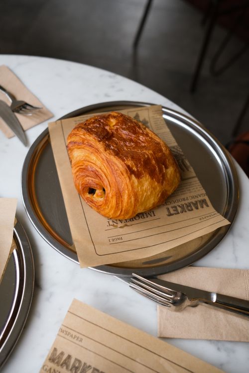 Free A flaky croissant served on a newspaper-lined plate at a cozy cafe. Stock Photo