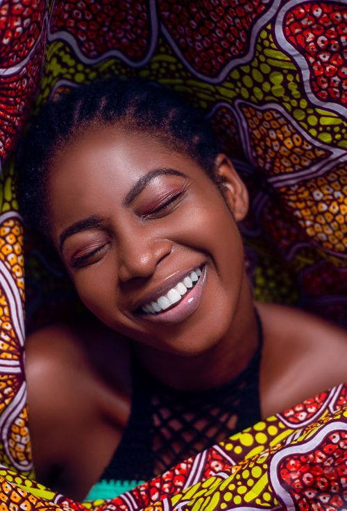 Free Smiling African woman surrounded by vibrant, patterned fabric in bright lighting. Stock Photo