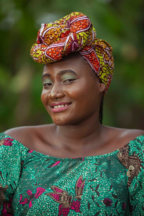 Free A smiling woman poses in a colorful African headwrap and dress outdoors. Stock Photo