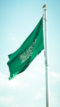 Vibrant Saudi Arabian flag waving high against a clear blue sky symbolizing national pride.