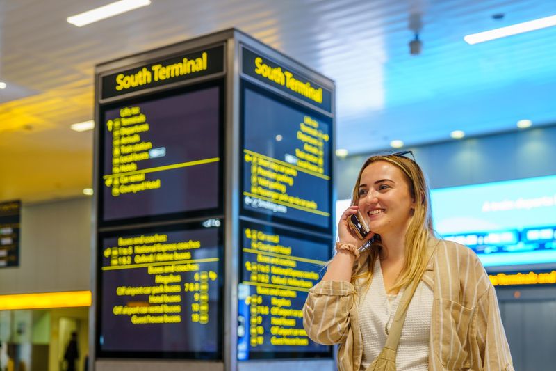 Smiling woman on phone in South Terminal of Gatwick Airport, Horley, enjoying her travel experience.