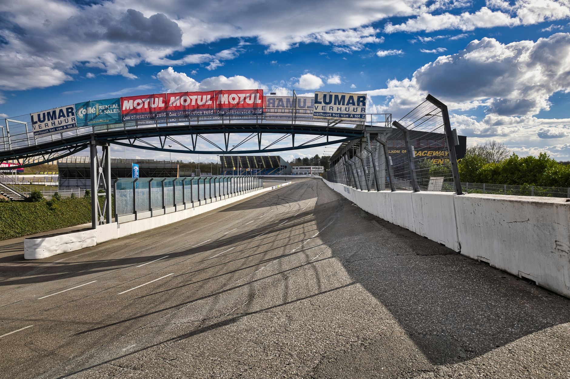 Deserted racetrack with overhead advertising bridge, clear day with clouds.