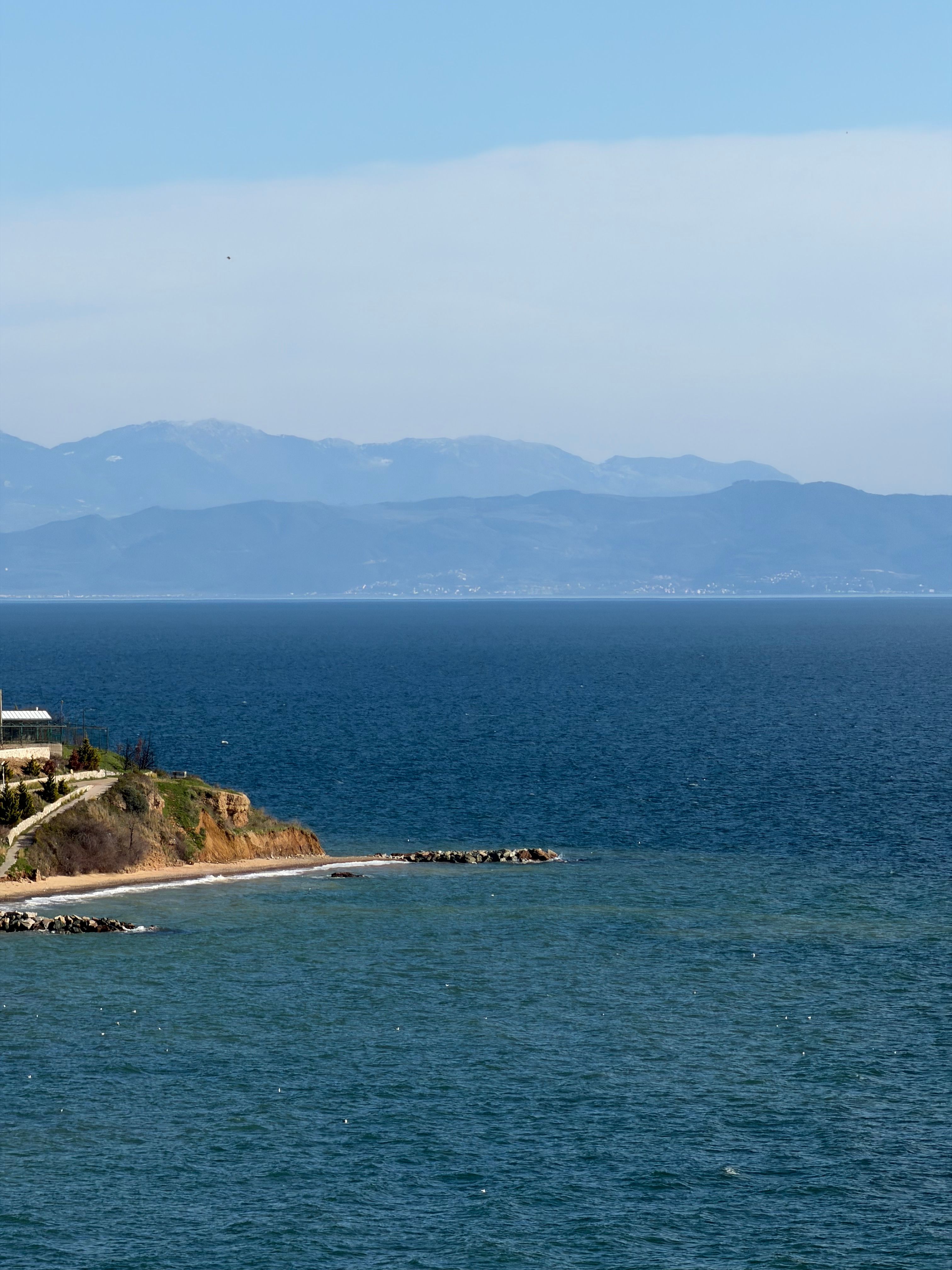 Serene coastal landscape with blue sea and distant mountains under clear sky.
