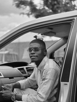 Black and white portrait of a man sitting in a car, wearing sunglasses.