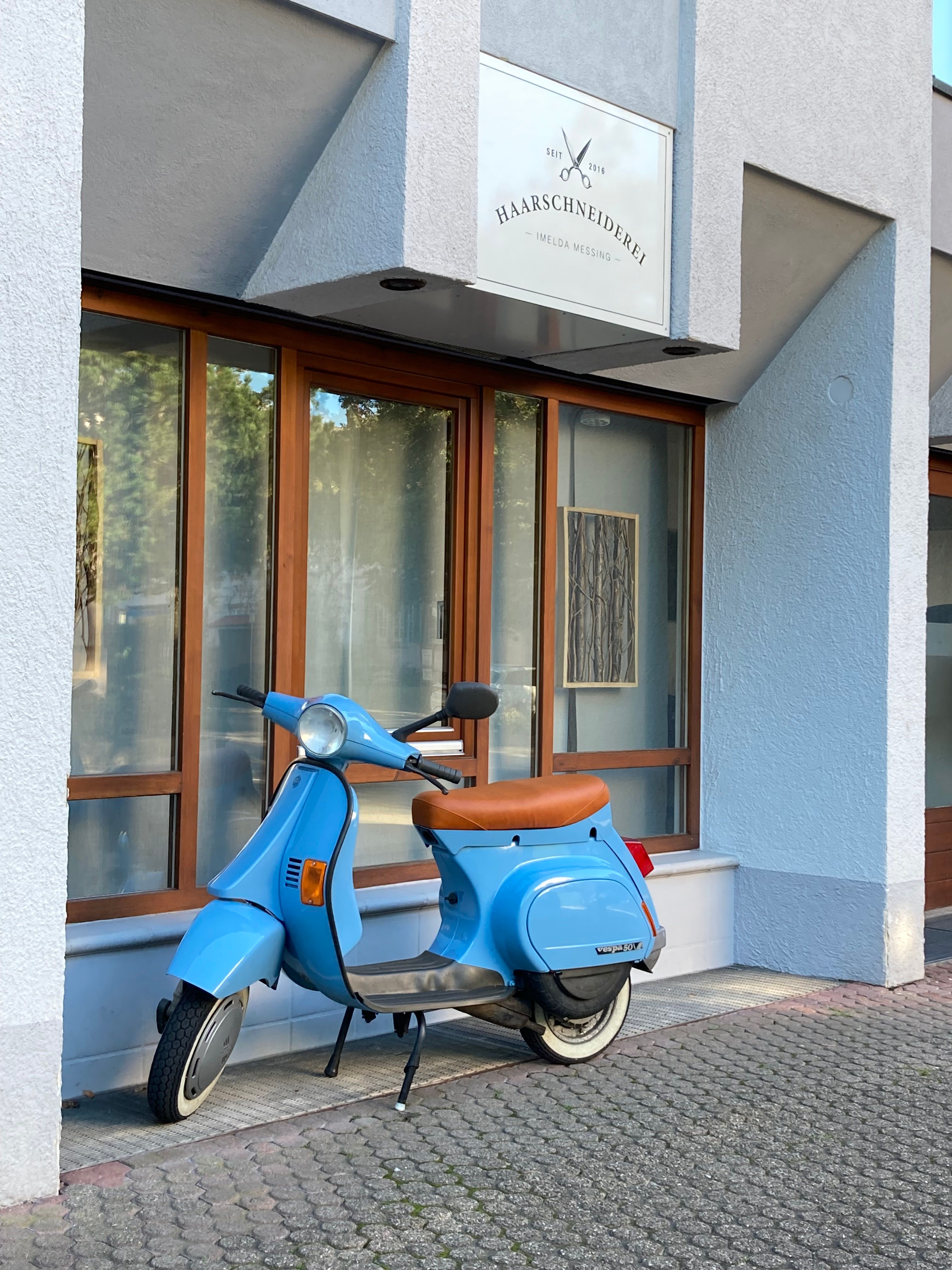 Stylish blue Vespa parked outside a modern hair salon facade, perfect for urban lifestyle themes.