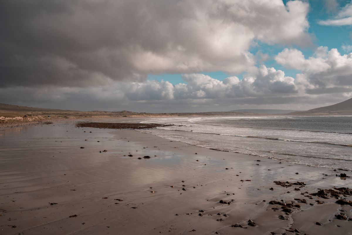 Longue plage de sable de l'Atlantique dans le comté de Kerry, sous un ciel nuageux, avec un promontoire montagneux à l'horizon