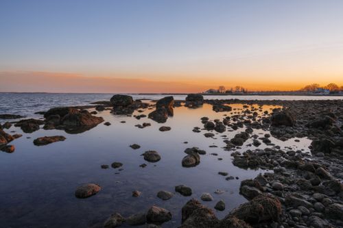 Free Peaceful sunset scene with rocky coastline reflecting vibrant colors in the calm waters. Stock Photo