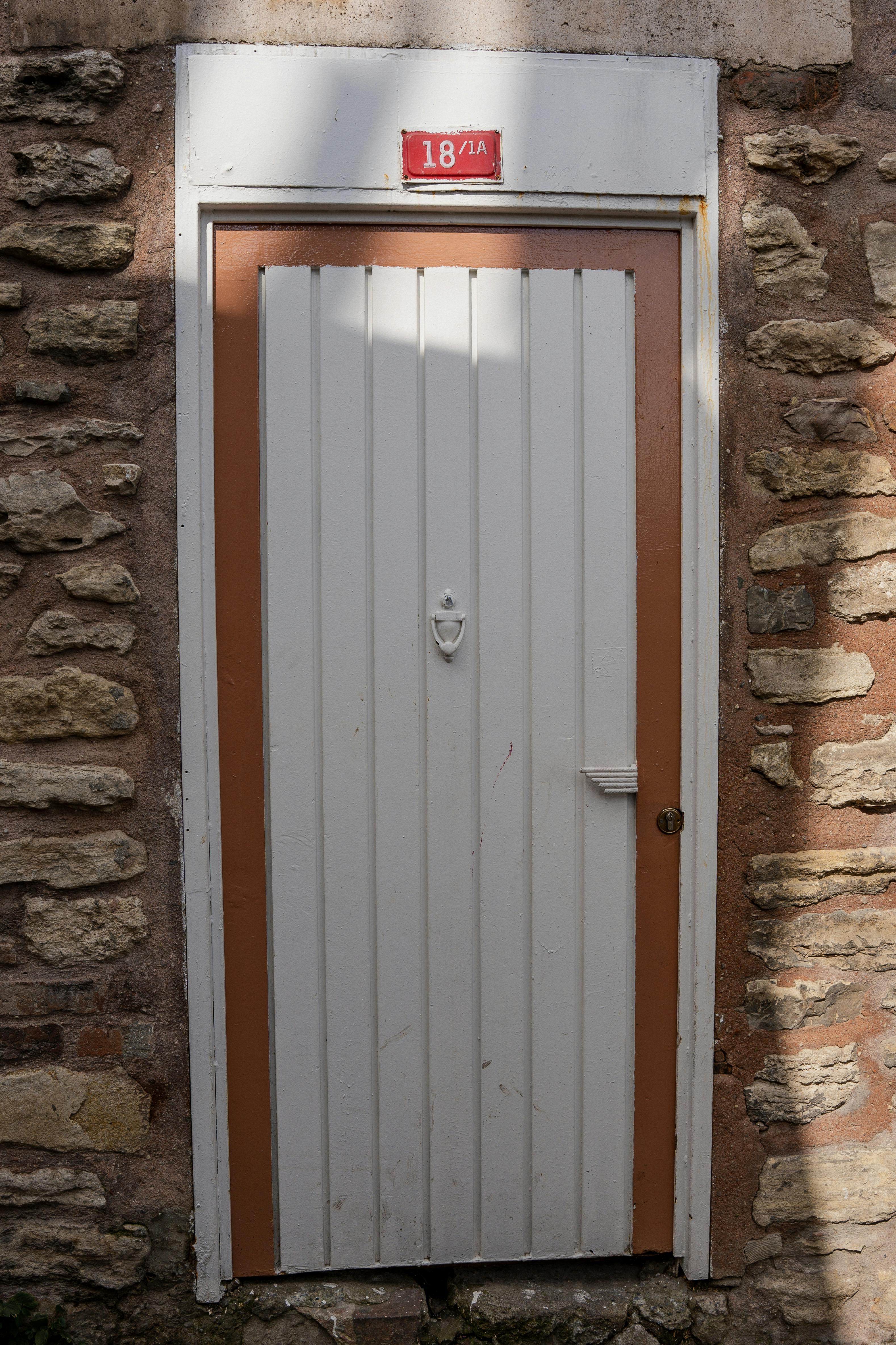 Gratis Hvit tredør satt i en rustikk steinvegg, med et rødt tallskilt. Arkivbilde