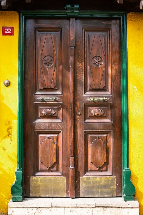 Free Charming rustic wooden door with intricate carvings on a vibrant yellow wall. Stock Photo