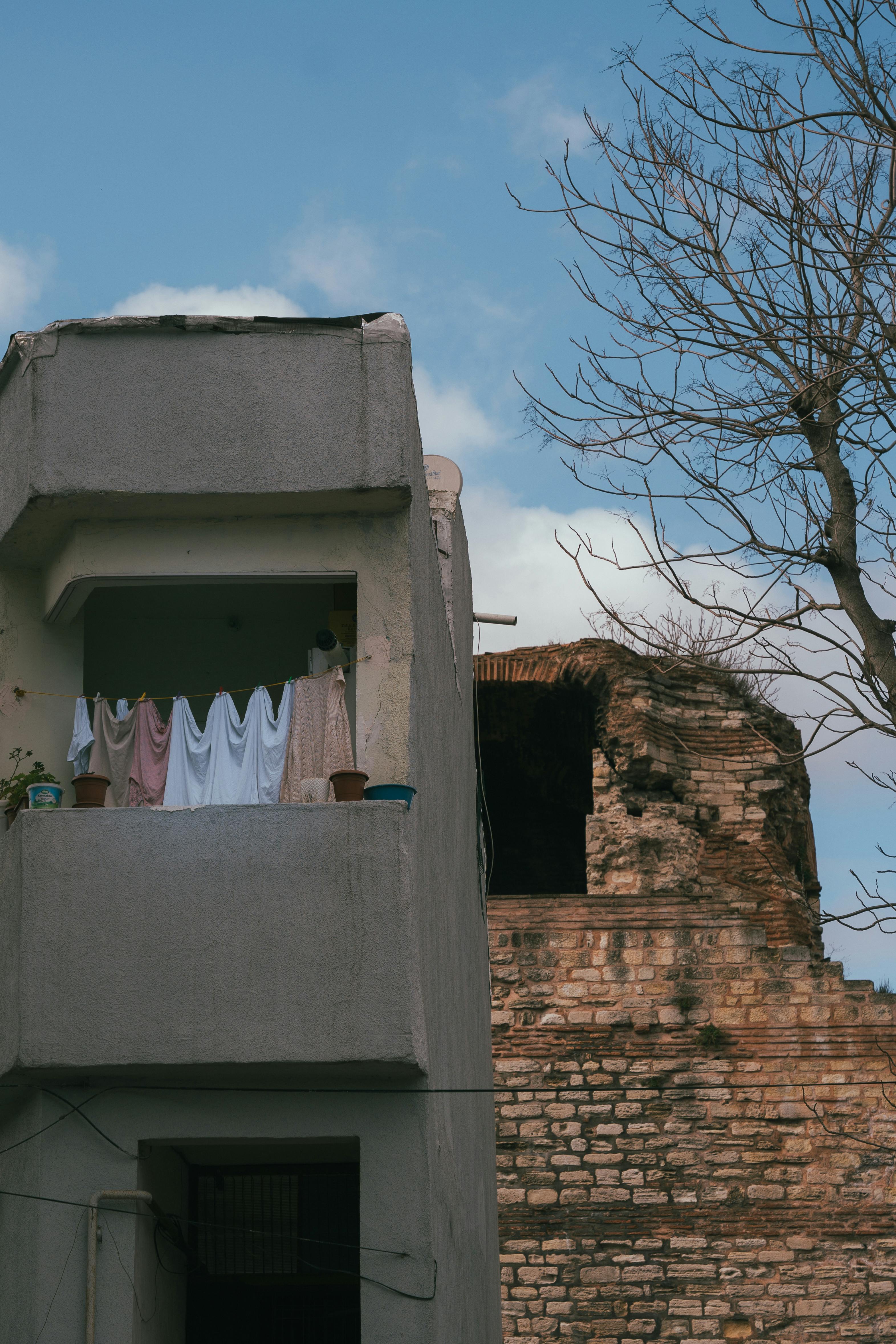 gratis Een grijs stadsbalkon met hangende was naast een oude bakstenen muur onder een blauwe hemel. Stockfoto