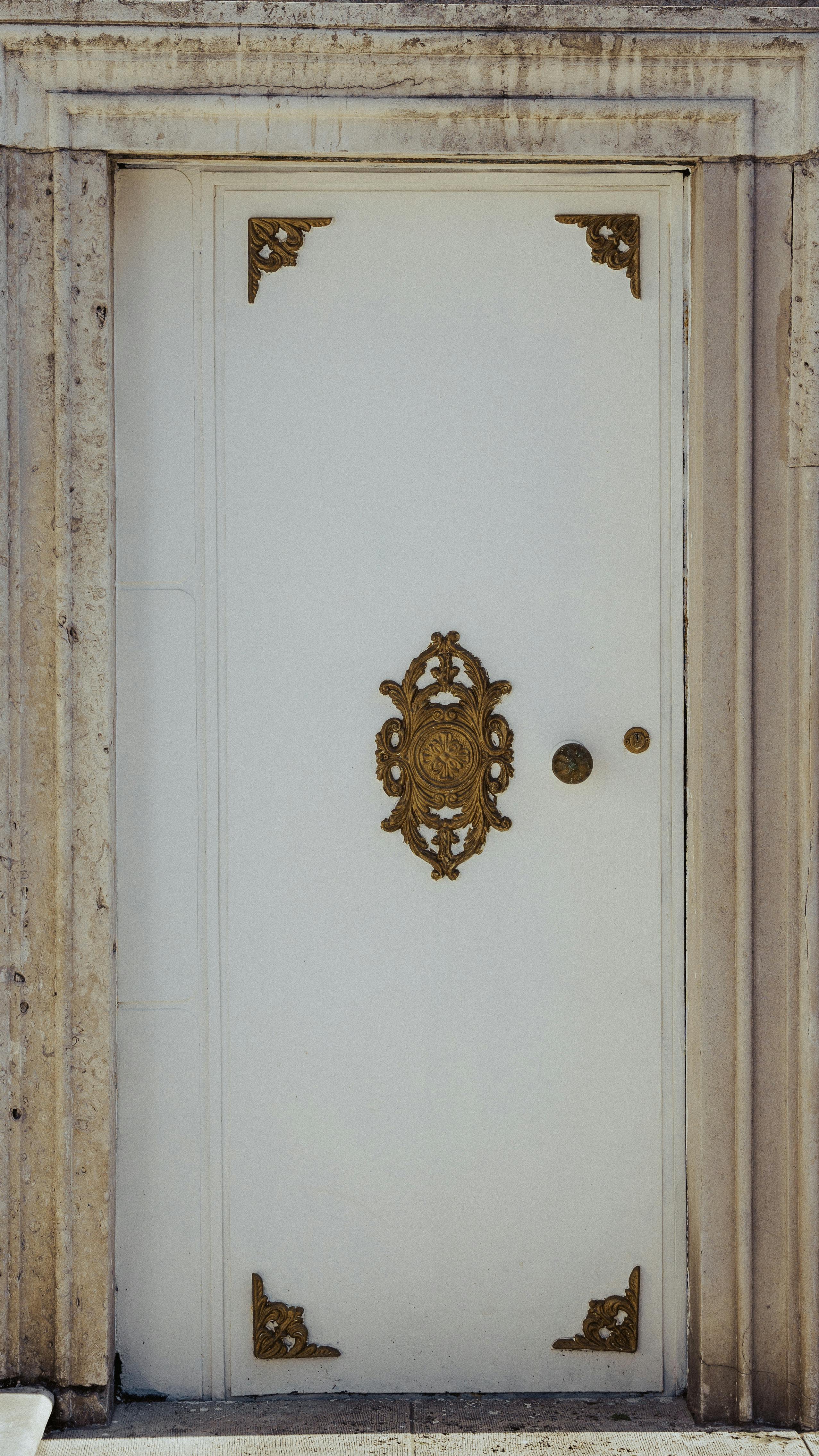 Free Elegant white door featuring intricate golden ornamental accents set in a vintage stone frame. Stock Photo