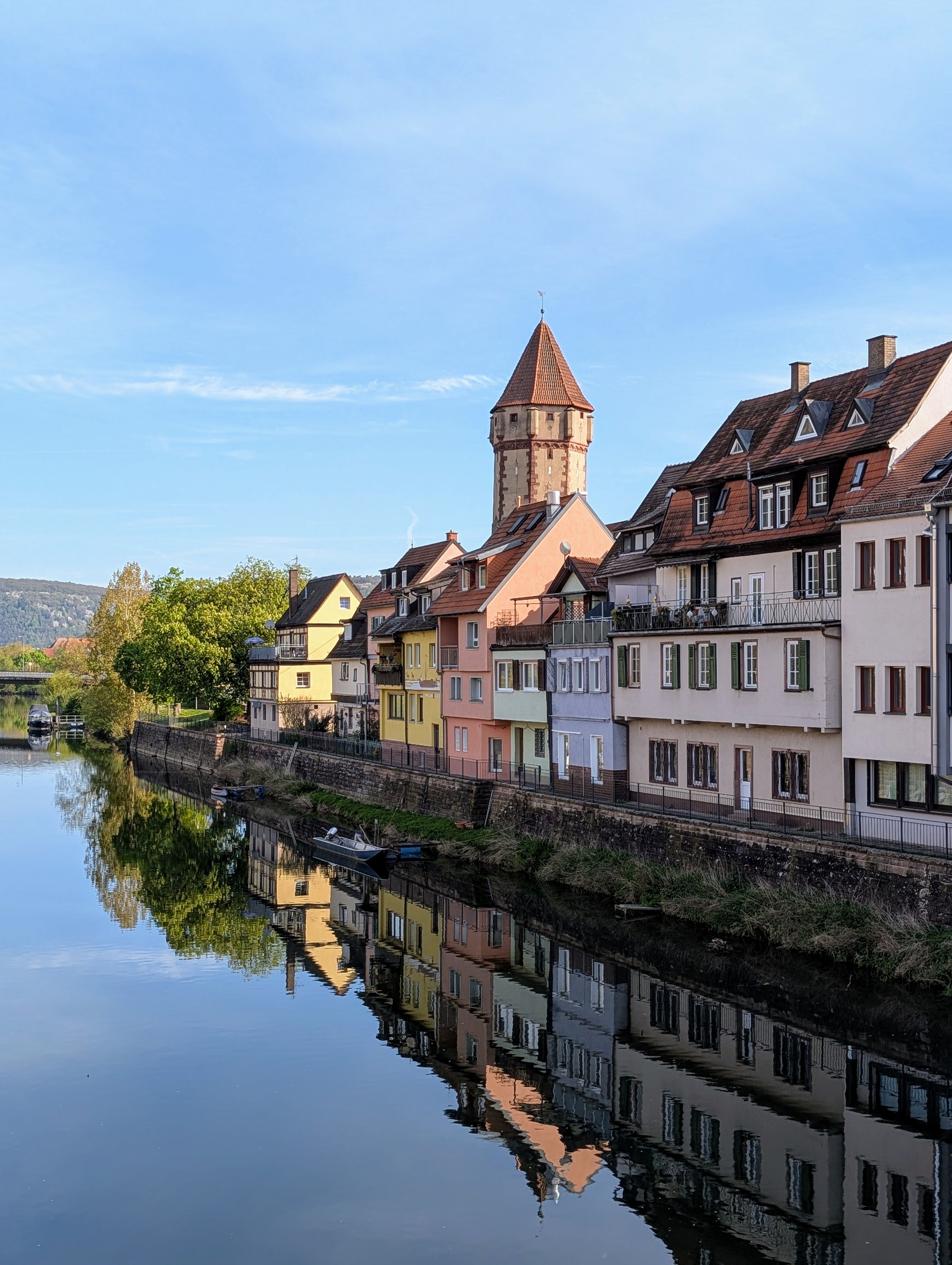Picturesque European village with colorful houses reflected in calm river water under blue sky.