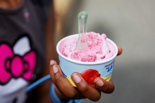 Hand holding pink ice cream in a cup with a spoon. Perfect for dessert-themed photography.