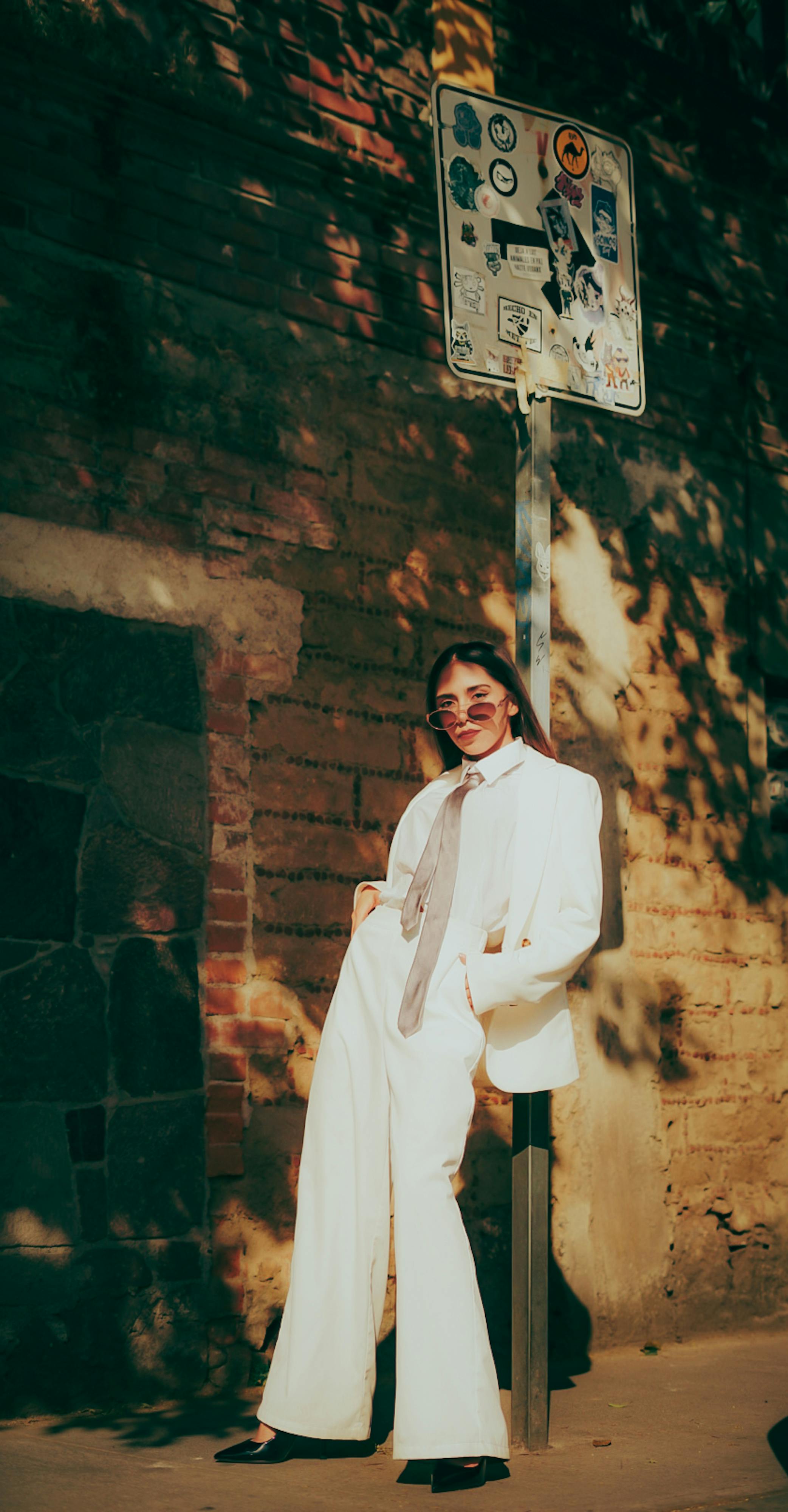 бесплатная Стильная женщина в белом костюме позирует на фоне фактурной кирпичной стены на залитой солнцем городской улице. Стоковое фото