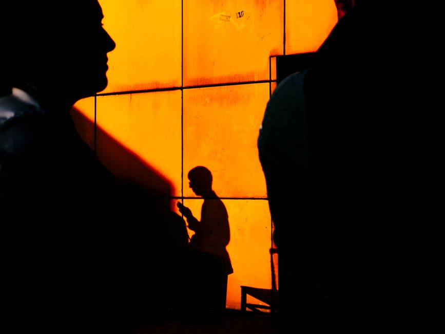 Artistic silhouettes cast on a vibrant orange wall in Istanbul, capturing urban life.