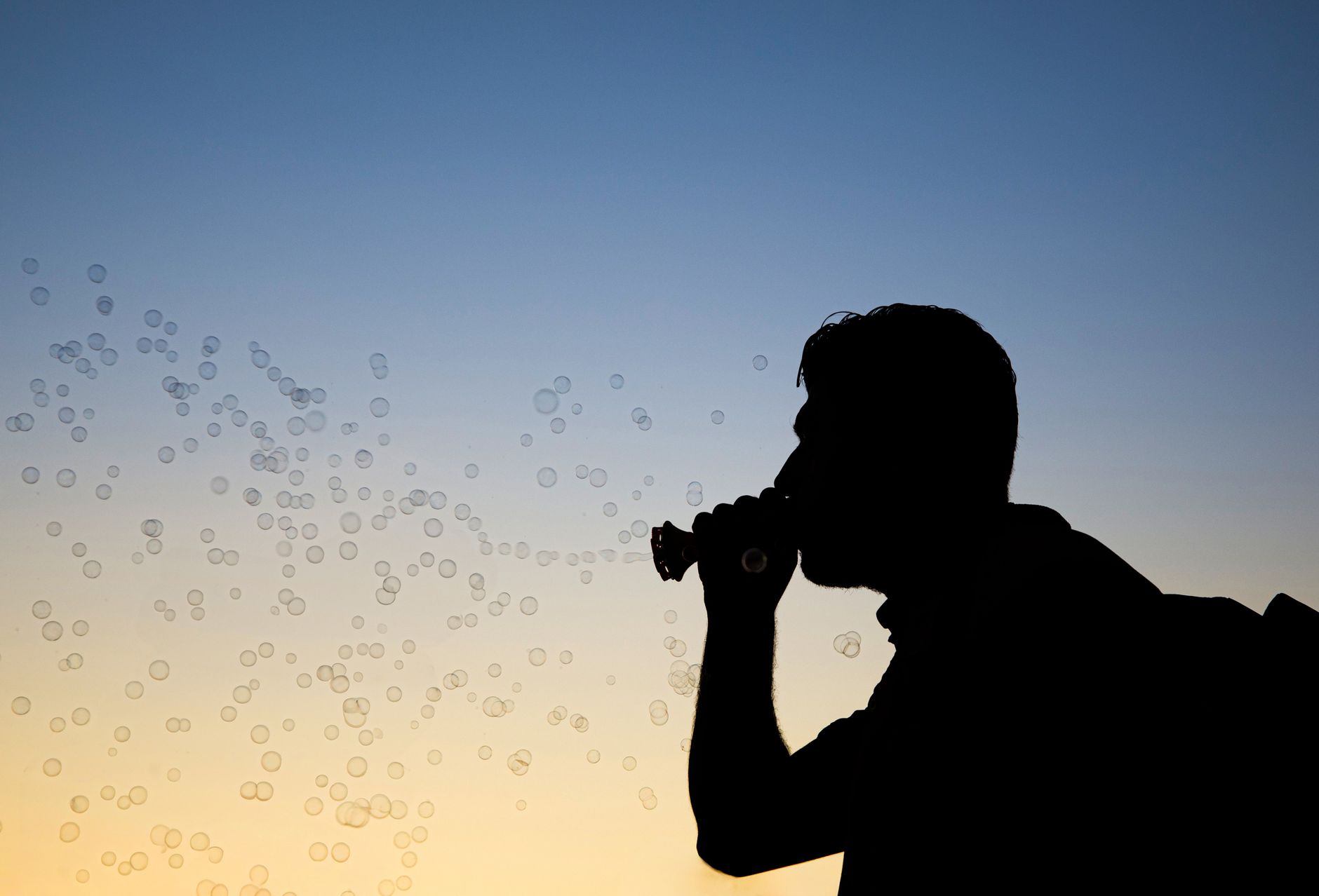 A man silhouetted against the sunset sky while blowing bubbles, creating a serene and playful scene.
