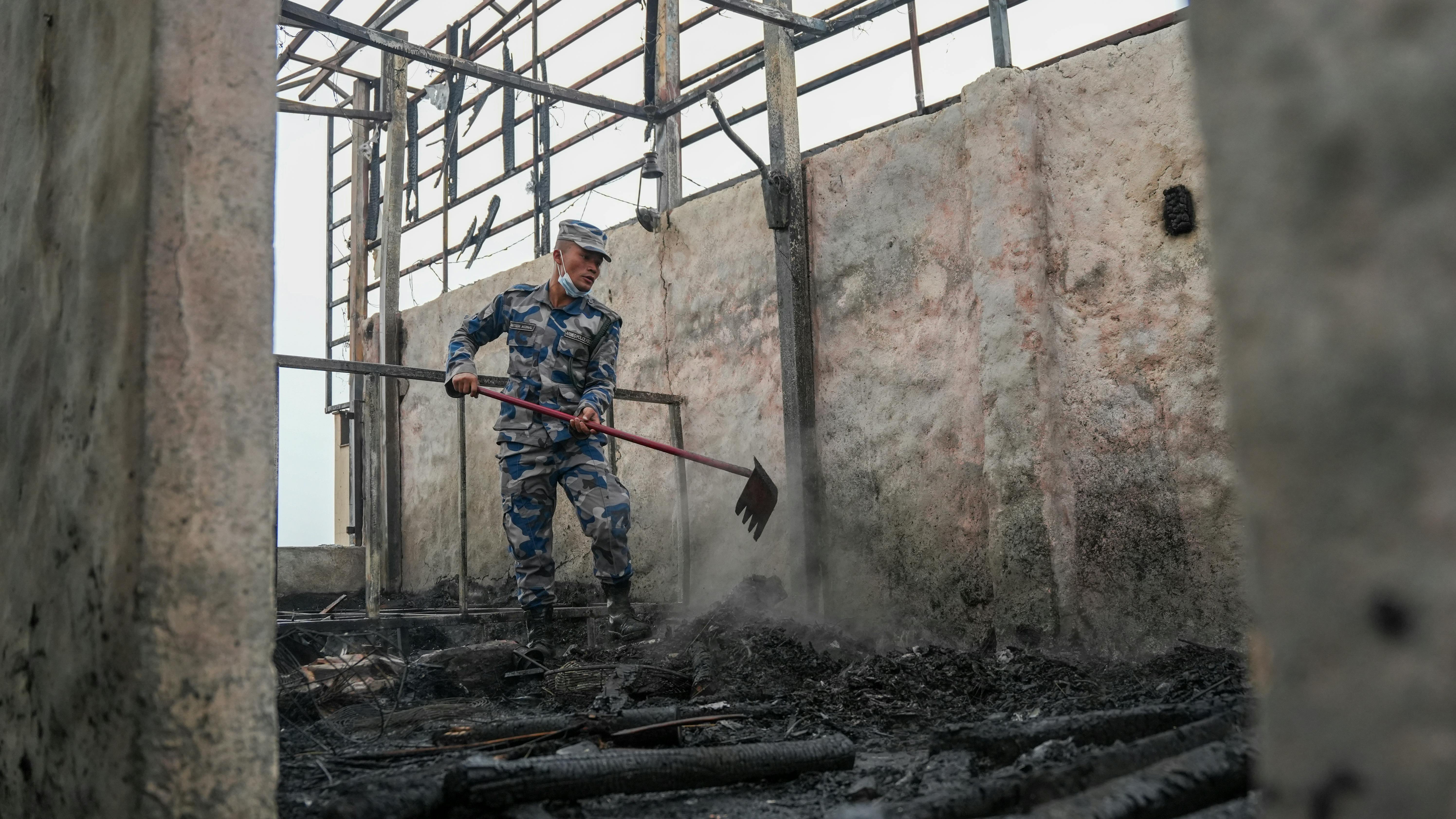 Firefighter in camouflage uniform cleaning debris in a burnt building, showcasing post-fire aftermath.