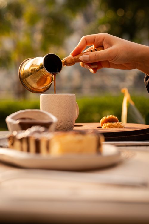 Free Hand pouring Turkish coffee into a cup with pastries outside, warm tones. Stock Photo