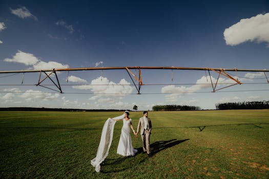 Bride and groom walk together under a clear blue sky on their wedding day in an open field.