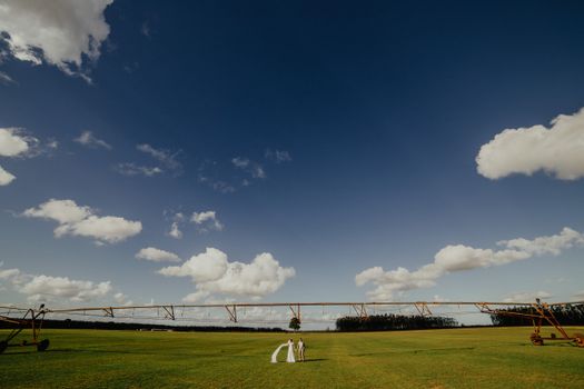 Bride and groom walking hand in hand in a vast green field with a stunning blue sky background.
