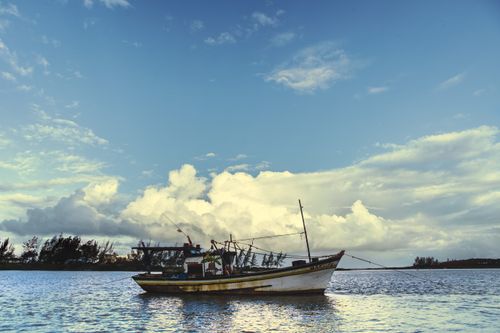 Free A peaceful fishing boat floats on calm waters under a vast blue sky. Stock Photo