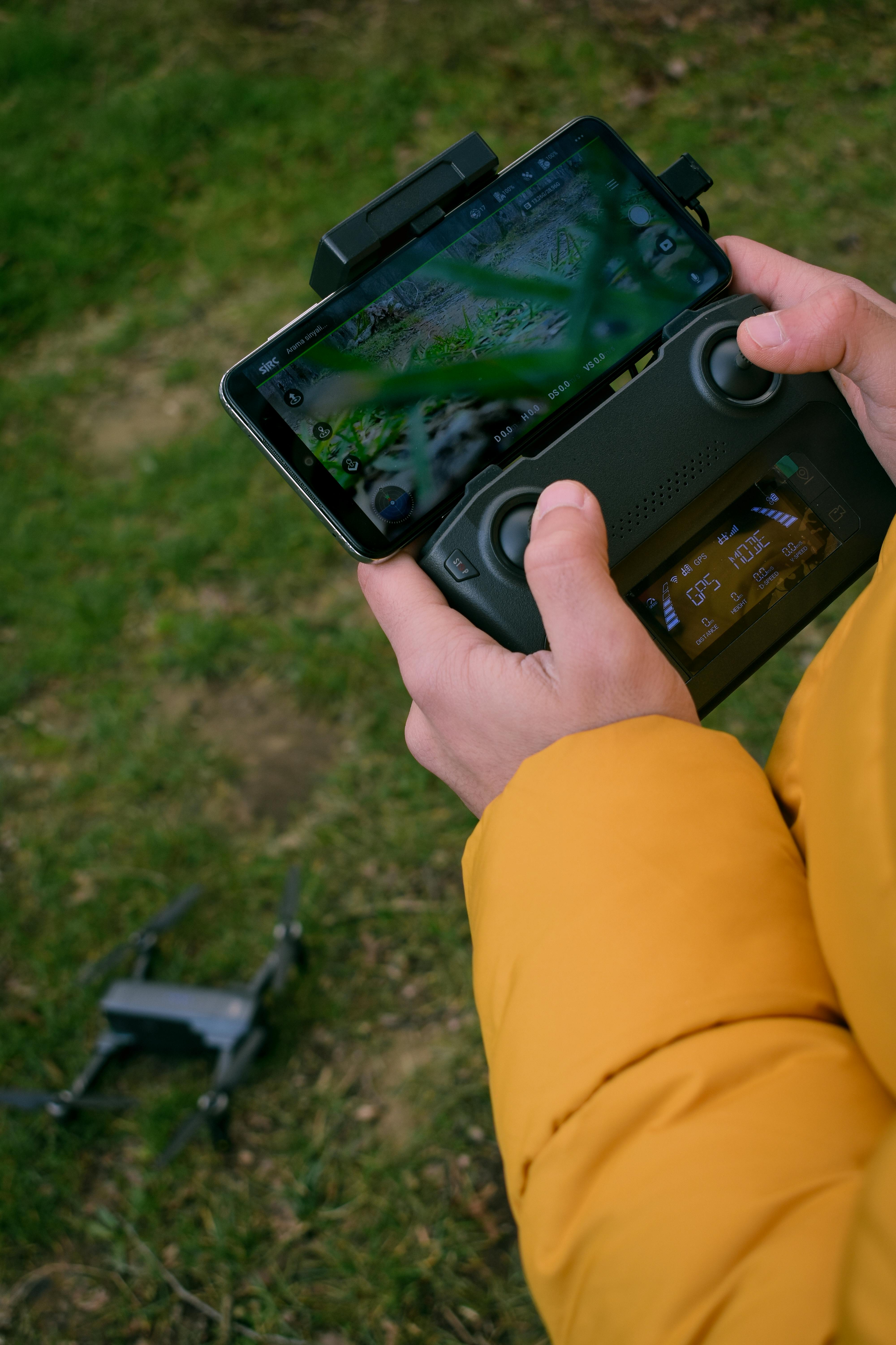 бесплатная Крупный план рук, управляющих дроном с помощью смартфона на открытом воздухе. Стоковое фото