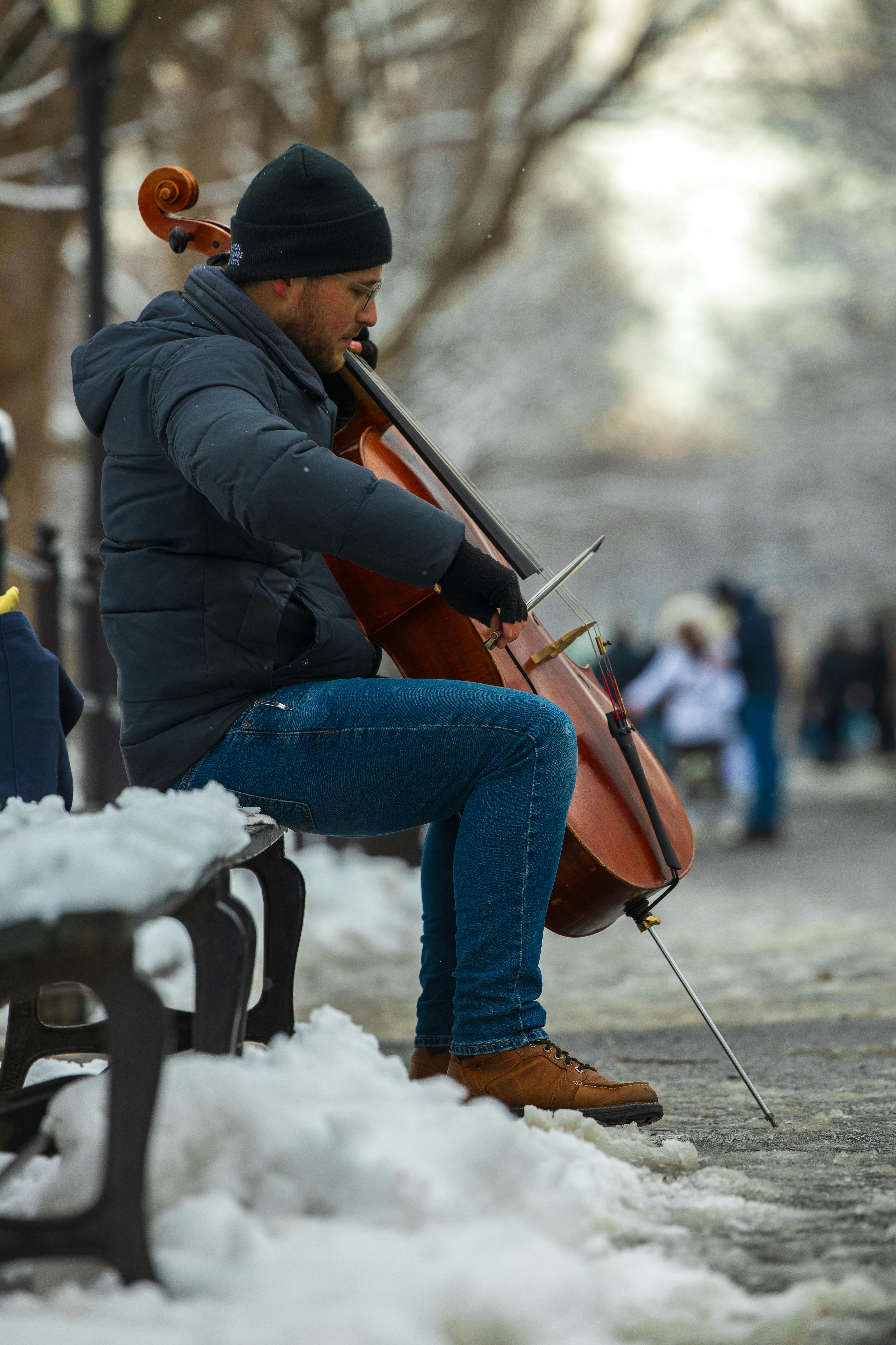 бесплатная Уличный музыкант играет на виолончели в заснеженном Центральном парке Нью-Йорка. Стоковое фото